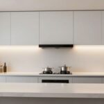 A professional, brightly lit modern kitchen featuring integrated, seamless LED under cabinet lighting that provides even coverage across the countertop.