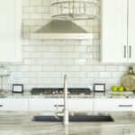 White subway tile kitchen backsplash running from the countertop up to white shaker upper cabinets and a stainless hood
