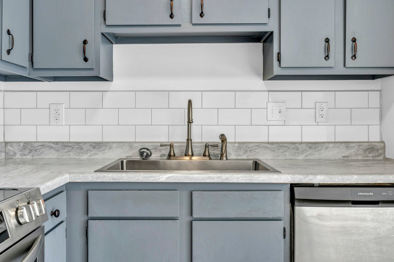 White subway tile filling the gap between a grey-veined countertop and grey upper cabinets, with outlets set in the tile