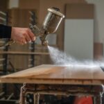 Spray gun applying a topcoat to a wood panel in a finishing shop