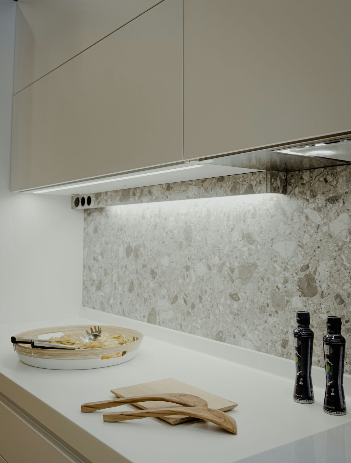 Outlets mounted under the upper cabinets with an LED strip above a terrazzo backsplash and white countertop