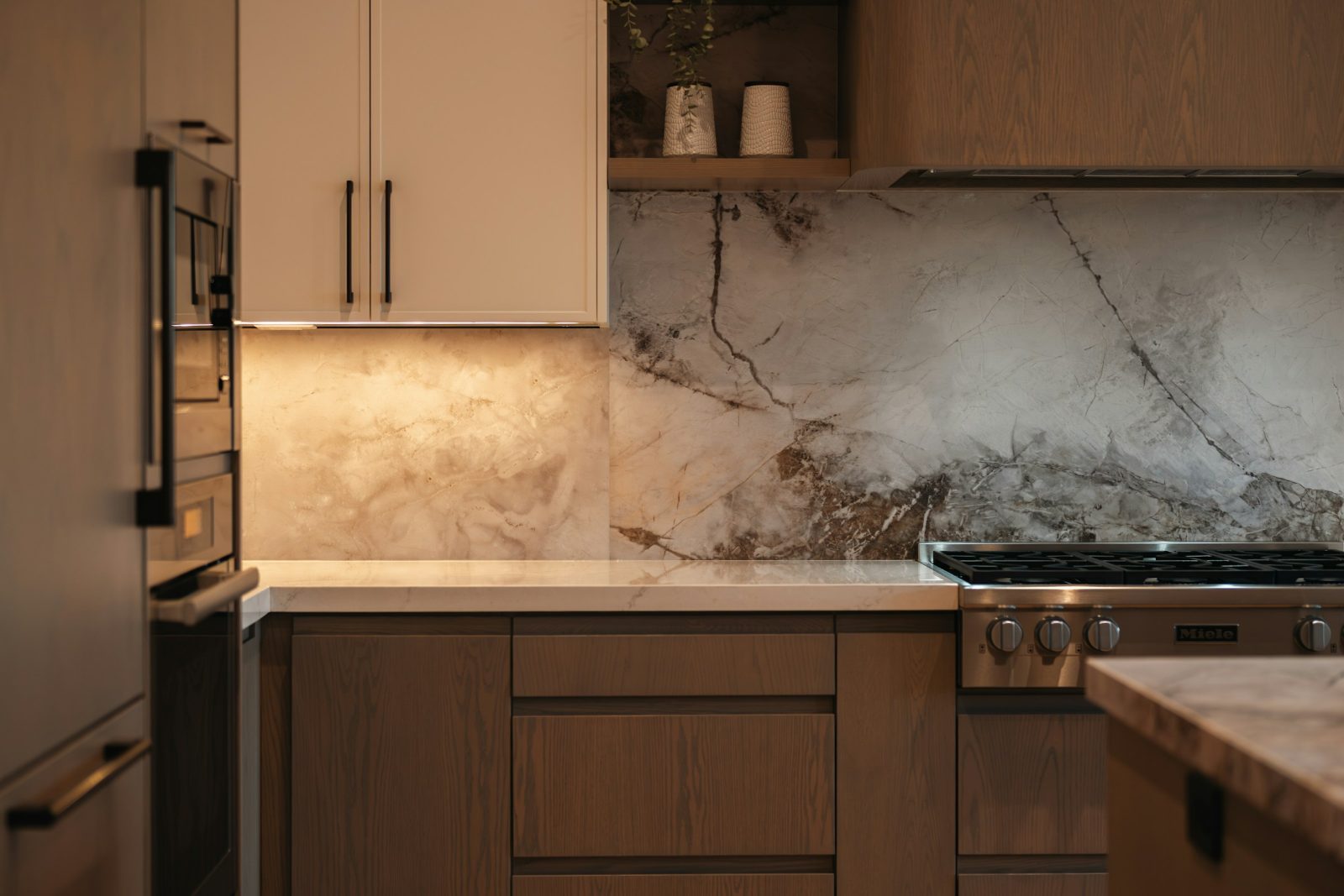 Full-height marble slab backsplash behind a gas range, with warm wood lower cabinets