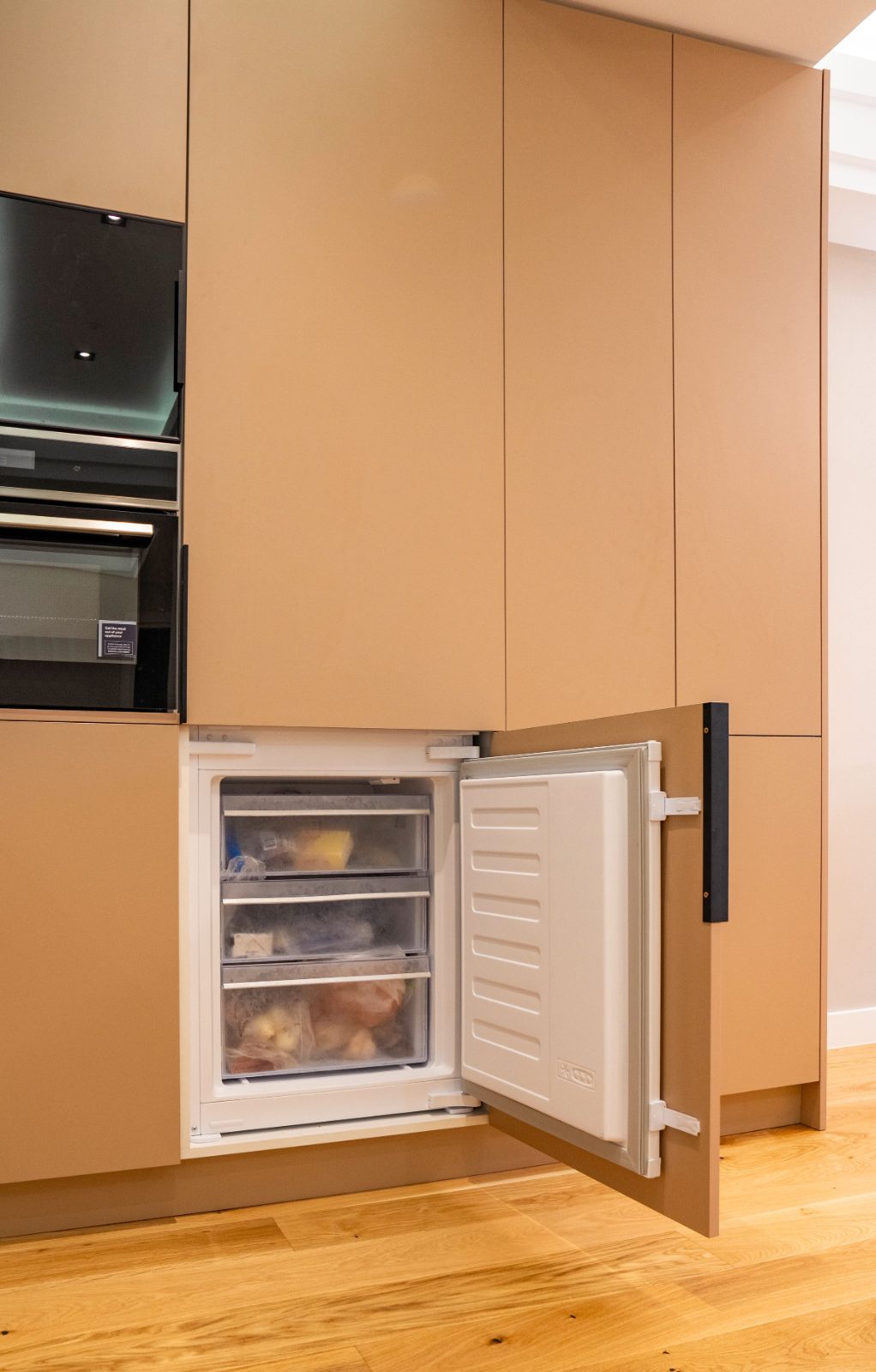 Panel-ready integrated freezer with its wood cabinet door open in a tall kitchen wall
