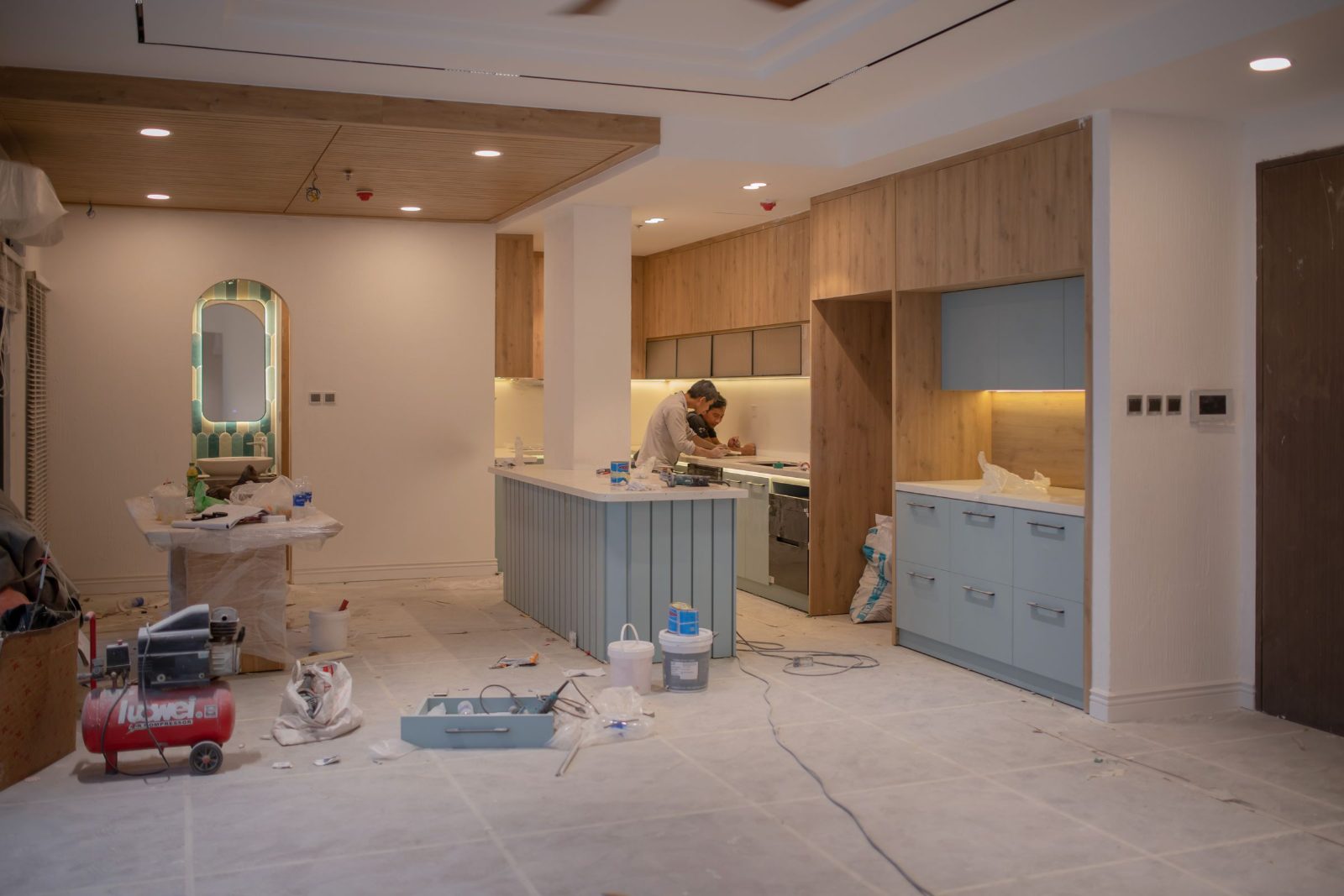 Kitchen cabinets partway through installation, with an installer at work and tools on the floor