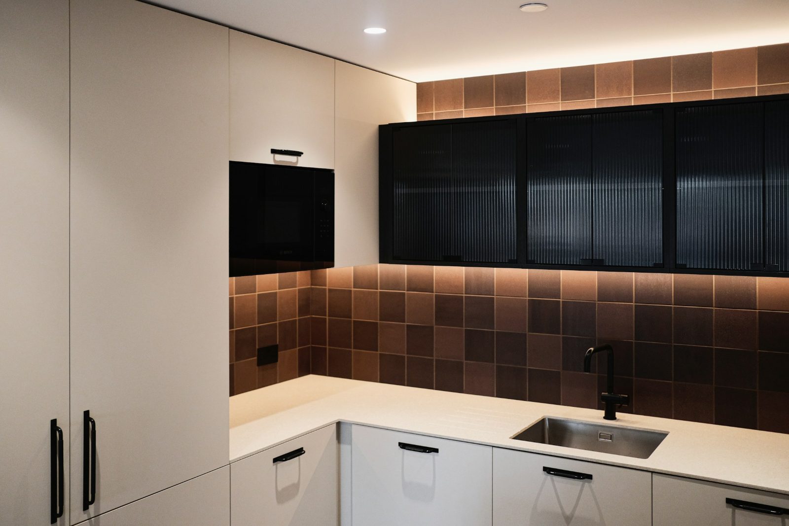LED strip lighting under black glass-front upper cabinets lighting up a brown tile backsplash